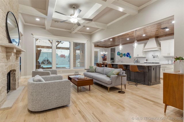 living room featuring coffered ceiling, ceiling fan, a stone fireplace, and light hardwood / wood-style flooring