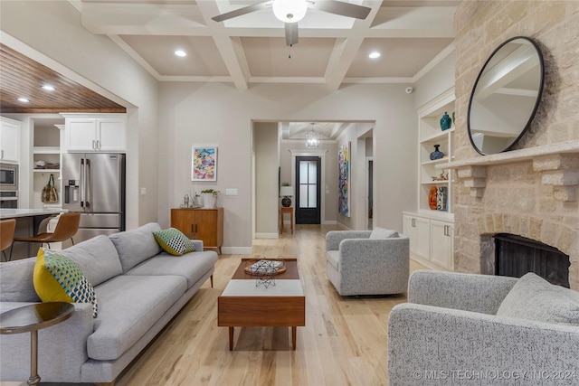 living room with coffered ceiling, a stone fireplace, ceiling fan, beamed ceiling, and light hardwood / wood-style floors