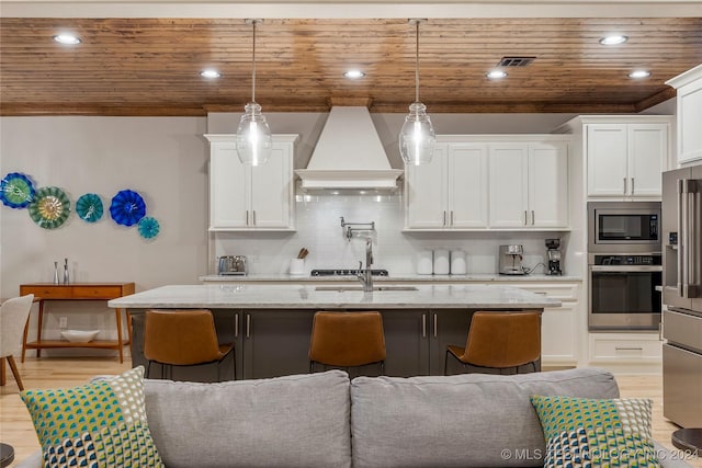 kitchen with light stone countertops, decorative light fixtures, stainless steel appliances, and custom range hood