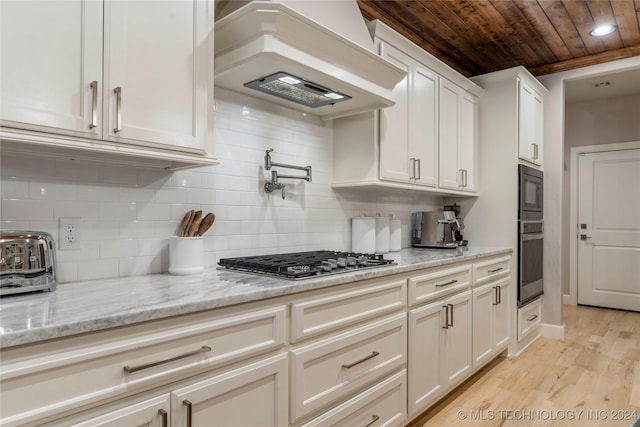 kitchen with light stone countertops, custom exhaust hood, stainless steel gas cooktop, light hardwood / wood-style flooring, and white cabinets