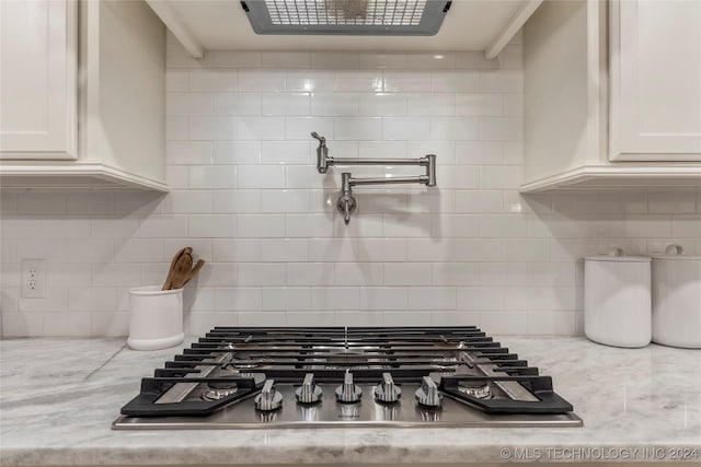 room details featuring white cabinets, light stone counters, stainless steel gas cooktop, and tasteful backsplash