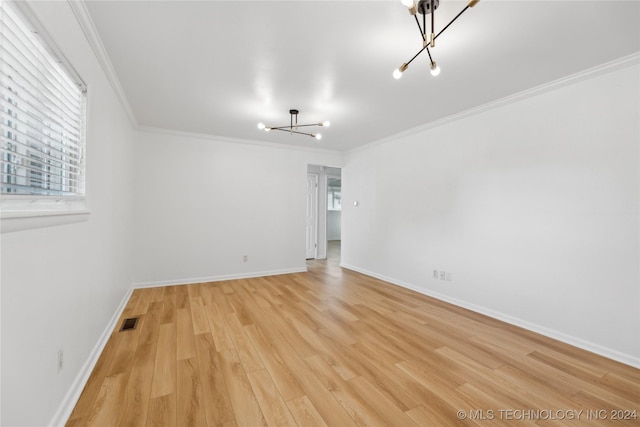 empty room with a notable chandelier, crown molding, and light hardwood / wood-style flooring