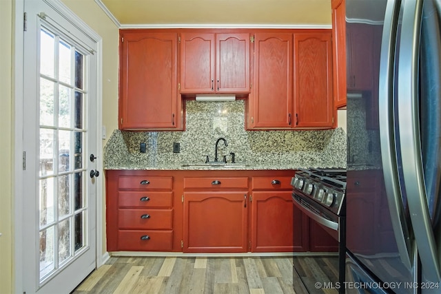 kitchen featuring stainless steel refrigerator, sink, black range with gas stovetop, light stone counters, and light hardwood / wood-style flooring