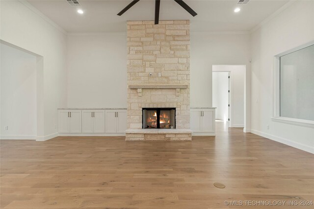 unfurnished living room featuring light wood-type flooring, a stone fireplace, ceiling fan, and crown molding