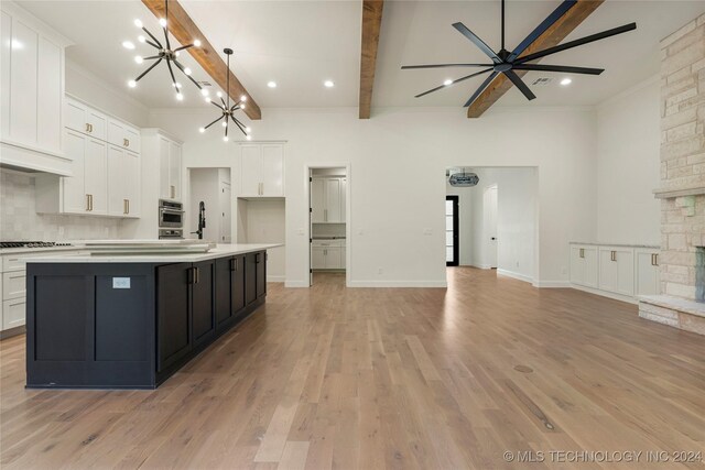 kitchen featuring a stone fireplace, white cabinetry, a center island with sink, and light wood-type flooring