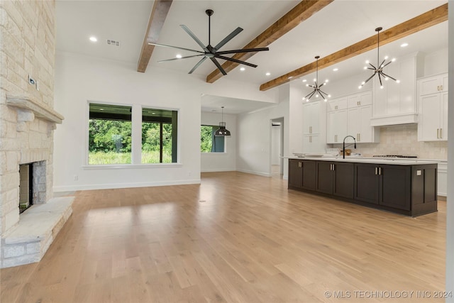 unfurnished living room with ceiling fan with notable chandelier, a stone fireplace, sink, light hardwood / wood-style flooring, and beam ceiling