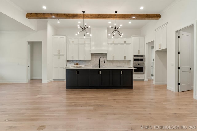 kitchen featuring a kitchen island with sink, beamed ceiling, hanging light fixtures, and light hardwood / wood-style floors