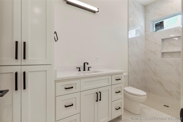 bathroom with a tile shower, vanity, and toilet