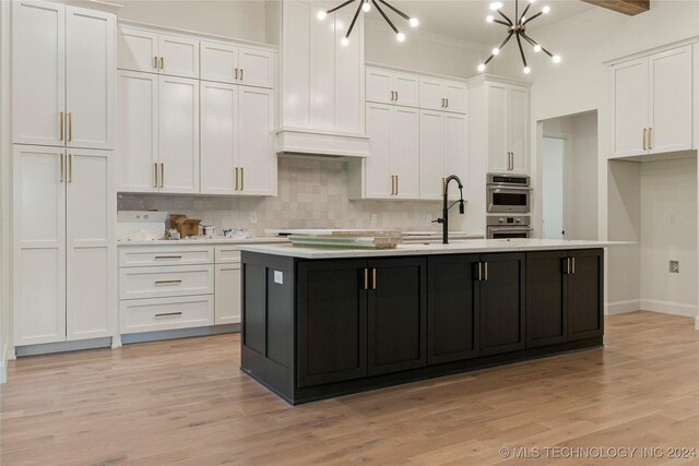 kitchen featuring white cabinets, an island with sink, a chandelier, and light wood-type flooring