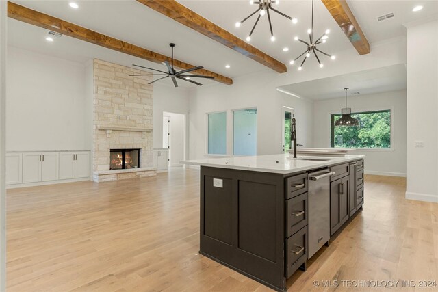 kitchen featuring a kitchen island with sink, sink, a fireplace, beamed ceiling, and light hardwood / wood-style floors