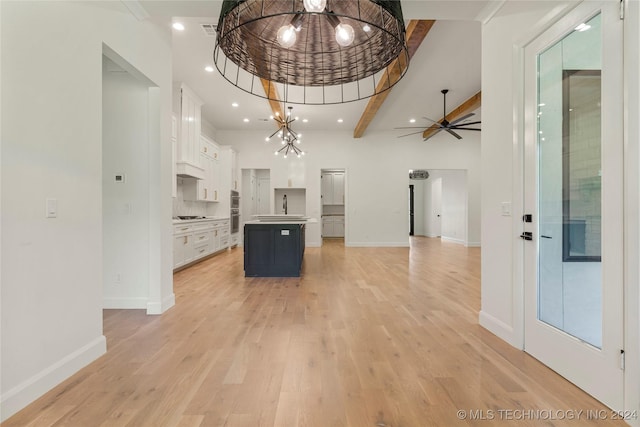 kitchen with ceiling fan with notable chandelier, light hardwood / wood-style floors, white cabinetry, and a kitchen island with sink