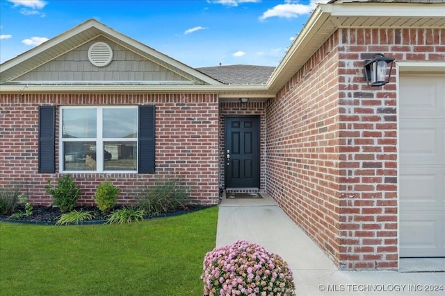 view of exterior entry featuring a garage and a lawn