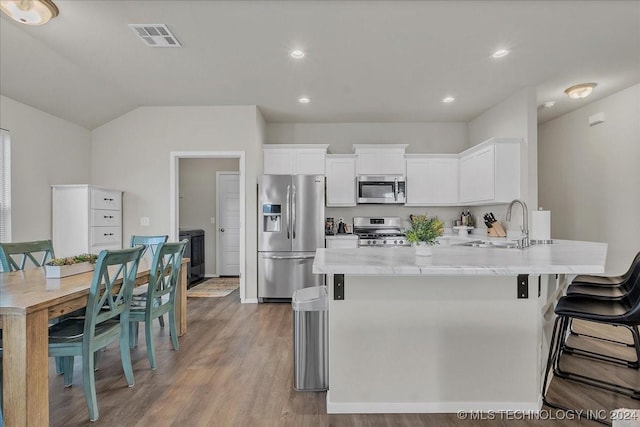 kitchen with appliances with stainless steel finishes, white cabinetry, sink, light stone countertops, and light wood-type flooring