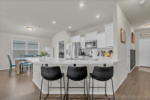 kitchen with appliances with stainless steel finishes, hardwood / wood-style floors, a breakfast bar area, white cabinets, and kitchen peninsula