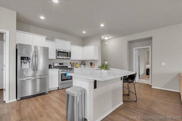 kitchen featuring stainless steel appliances, sink, white cabinets, light hardwood / wood-style floors, and a breakfast bar area