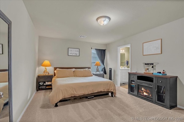 bedroom with ensuite bathroom and light carpet