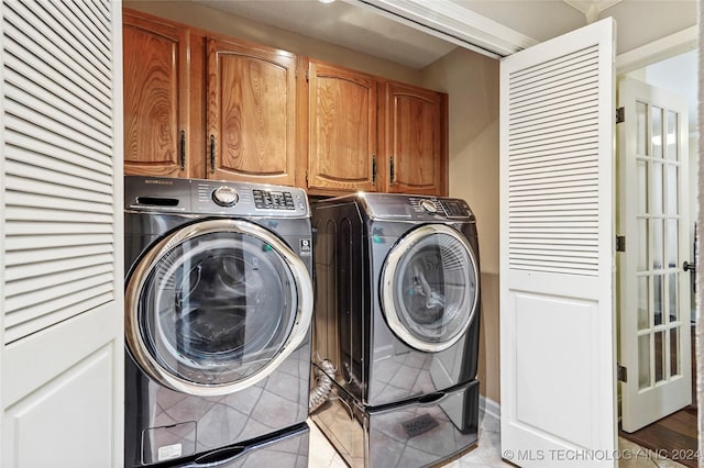 clothes washing area with cabinets, light tile patterned flooring, and washing machine and clothes dryer