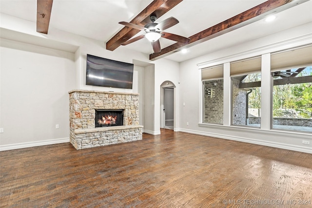 unfurnished living room with a stone fireplace, ceiling fan, beamed ceiling, and wood-type flooring