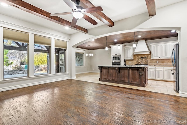 kitchen with light stone countertops, a kitchen bar, premium range hood, a center island with sink, and white cabinets