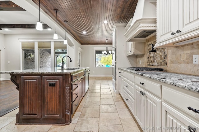 kitchen with sink, decorative backsplash, a center island with sink, white cabinets, and custom exhaust hood