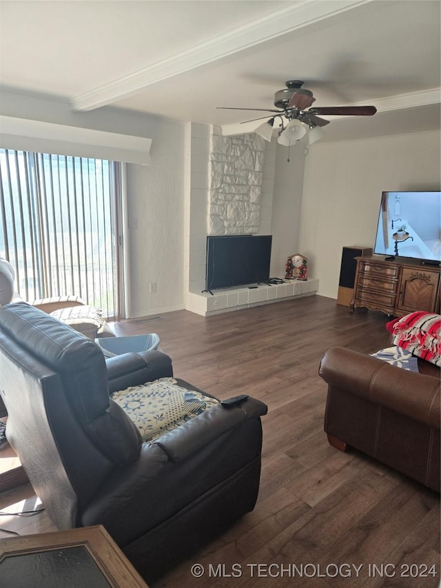 living room featuring beam ceiling, ceiling fan, a large fireplace, dark wood-type flooring, and ornamental molding