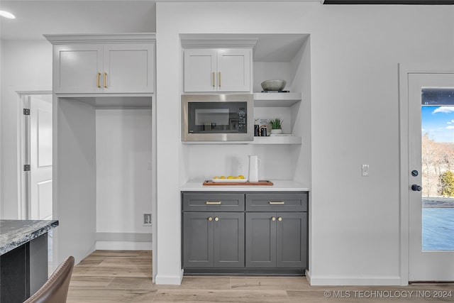 bar with light stone countertops, gray cabinets, built in microwave, and light hardwood / wood-style floors