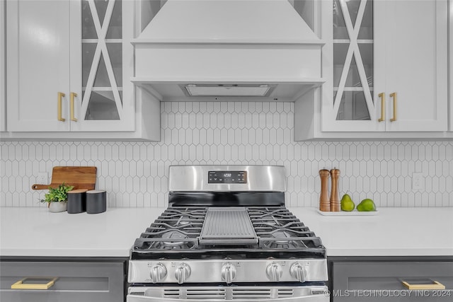 kitchen with tasteful backsplash, stainless steel gas range oven, white cabinetry, and custom exhaust hood