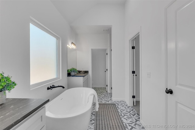 bathroom featuring visible vents, baseboards, a soaking tub, vanity, and vaulted ceiling