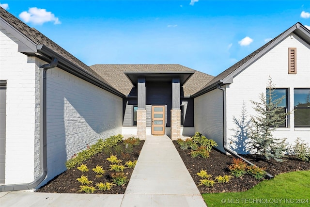 doorway to property with brick siding and roof with shingles