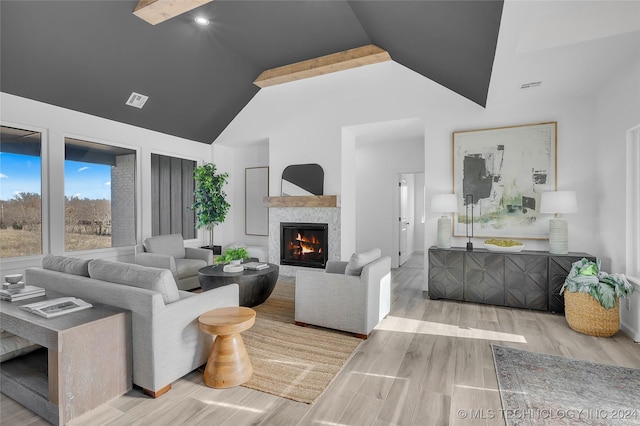 living area featuring vaulted ceiling, a glass covered fireplace, visible vents, and wood finished floors