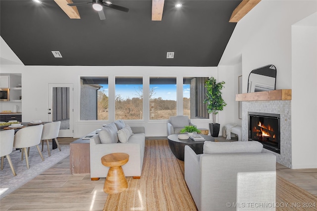 living room featuring beam ceiling, a tile fireplace, ceiling fan, light hardwood / wood-style flooring, and built in features