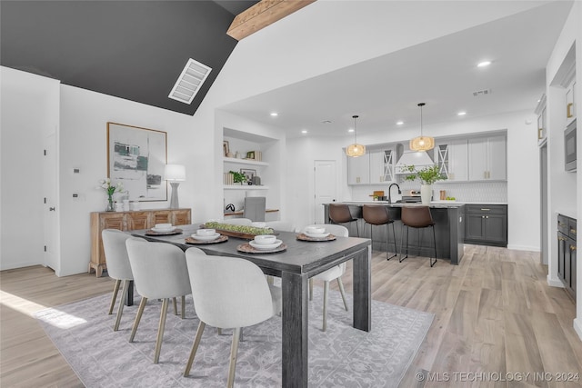 dining area featuring built in shelves, vaulted ceiling with beams, light hardwood / wood-style flooring, and sink