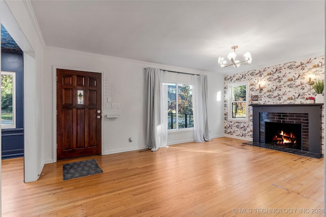 unfurnished living room with a fireplace, an inviting chandelier, light hardwood / wood-style flooring, and ornamental molding