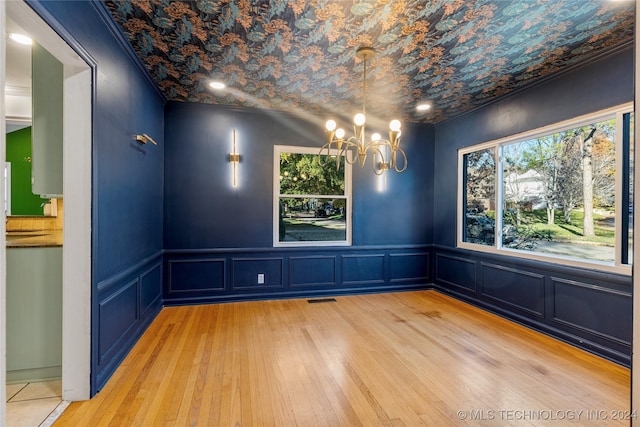 unfurnished dining area with a chandelier, light wood-type flooring, and ornamental molding