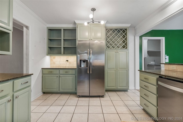 kitchen featuring appliances with stainless steel finishes, dark stone counters, crown molding, light tile patterned floors, and green cabinets