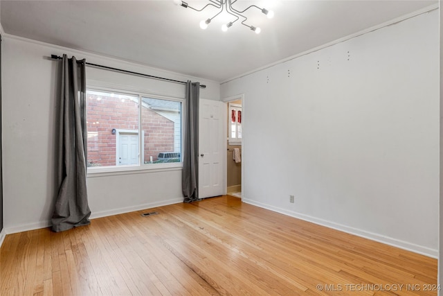 empty room featuring hardwood / wood-style flooring, crown molding, and an inviting chandelier