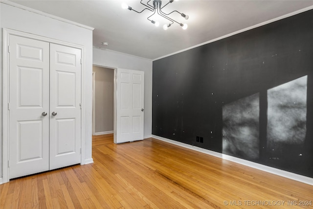 unfurnished bedroom with a chandelier, light hardwood / wood-style floors, ornamental molding, and a closet