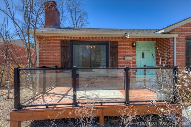 doorway to property featuring a shingled roof, a chimney, a deck, and brick siding