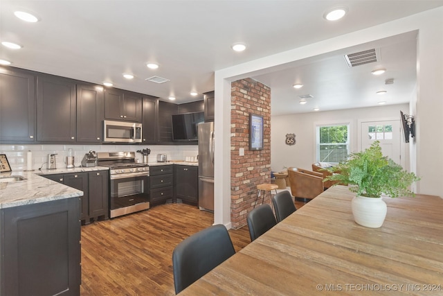 kitchen featuring light stone countertops, sink, hardwood / wood-style floors, decorative backsplash, and appliances with stainless steel finishes