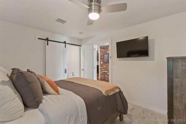 carpeted bedroom with a barn door, ceiling fan, and ensuite bathroom