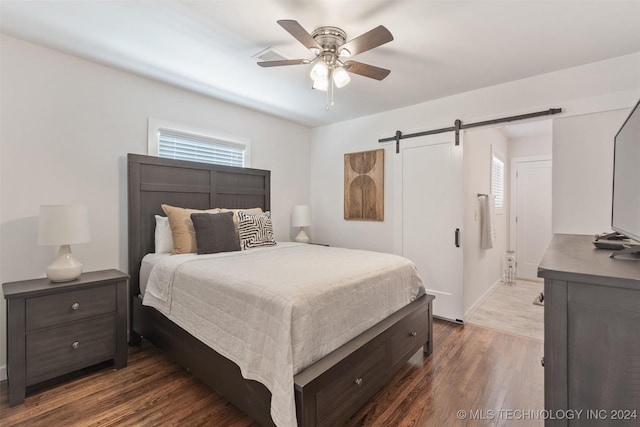 bedroom with a barn door, ceiling fan, and dark hardwood / wood-style floors