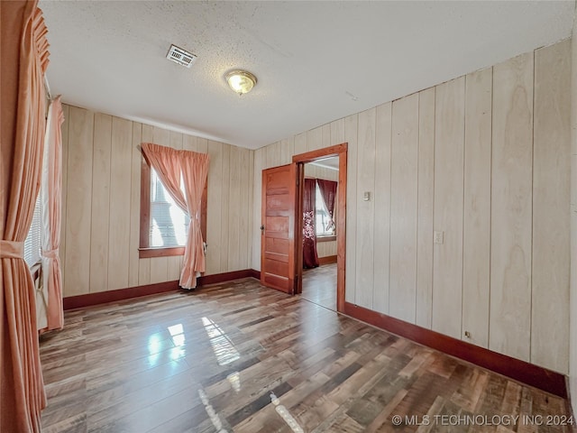 spare room with hardwood / wood-style floors, a textured ceiling, and wood walls