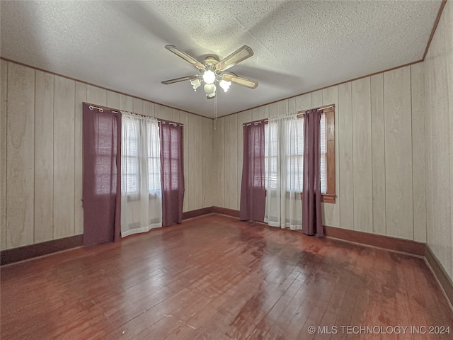 empty room featuring wooden walls, dark wood-type flooring, and a wealth of natural light