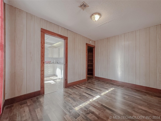 empty room with a textured ceiling, hardwood / wood-style flooring, and wooden walls