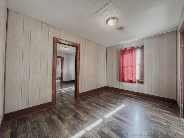 spare room featuring wooden walls, dark hardwood / wood-style flooring, and a textured ceiling