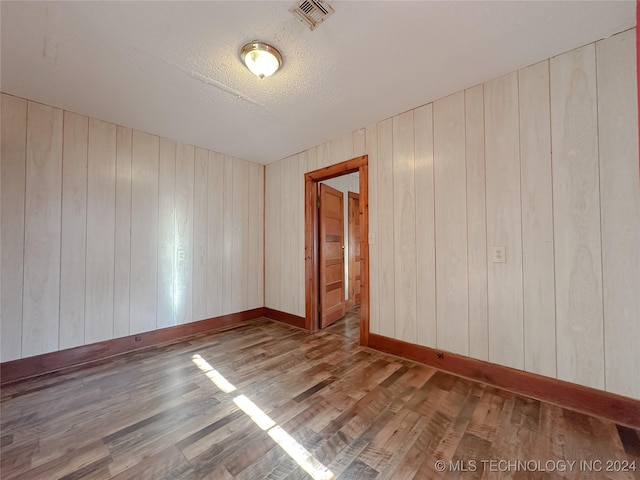 spare room featuring hardwood / wood-style floors, wood walls, and a textured ceiling