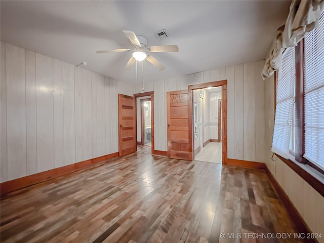 unfurnished room featuring a wealth of natural light, hardwood / wood-style floors, ceiling fan, and wood walls