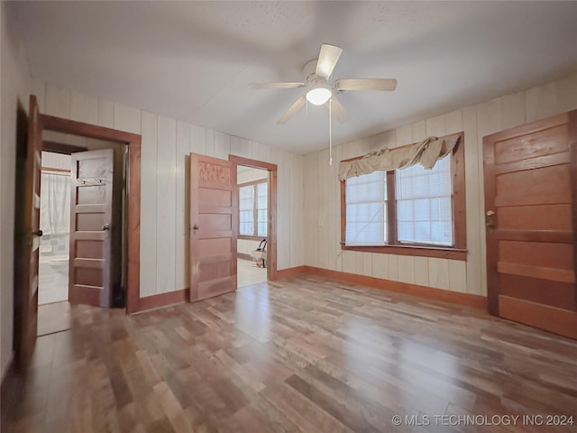 unfurnished room with ceiling fan, hardwood / wood-style floors, and wooden walls