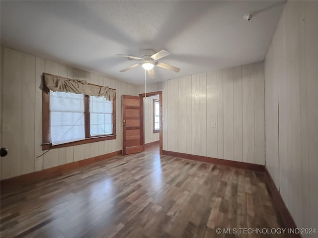 spare room featuring ceiling fan, wooden walls, and hardwood / wood-style flooring