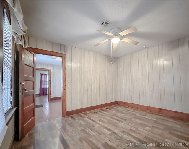 spare room with ceiling fan, wooden walls, and light hardwood / wood-style floors